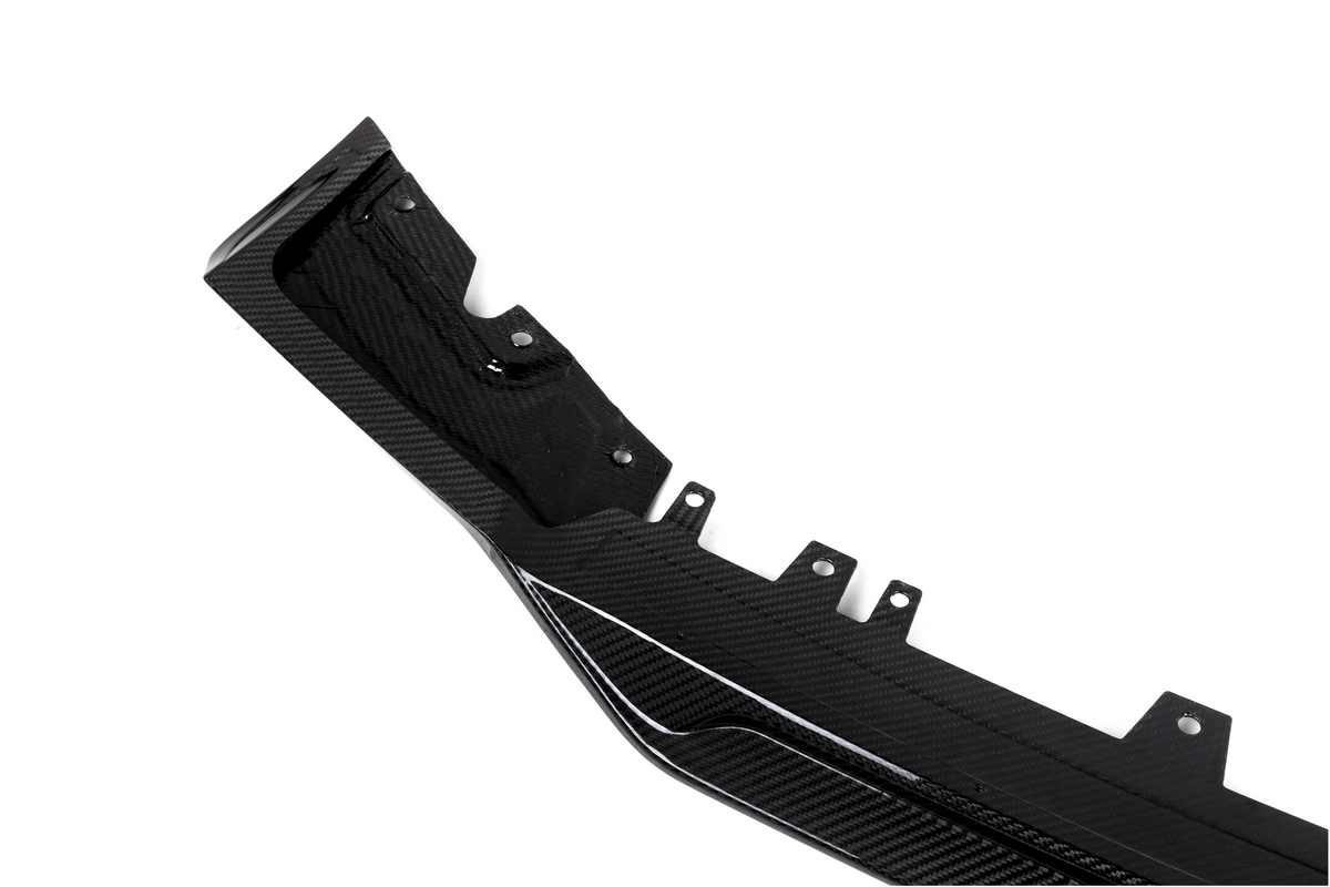 A black carbon fiber automotive component, featuring mounting points and textured patterns, lies against a plain white background.