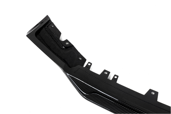 A black carbon fiber automotive component, featuring mounting points and textured patterns, lies against a plain white background.