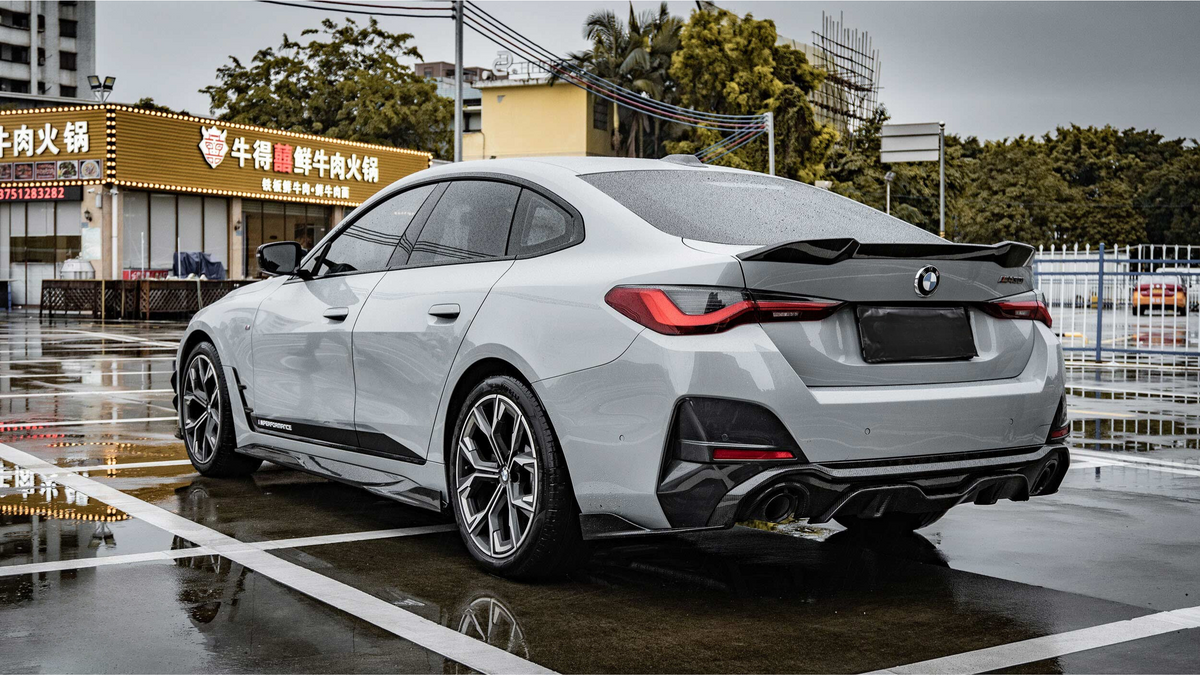 A silver car is parked on a wet pavement near a restaurant with illuminated signage in Chinese characters and telephone numbers: "0752323232" and "075523282".