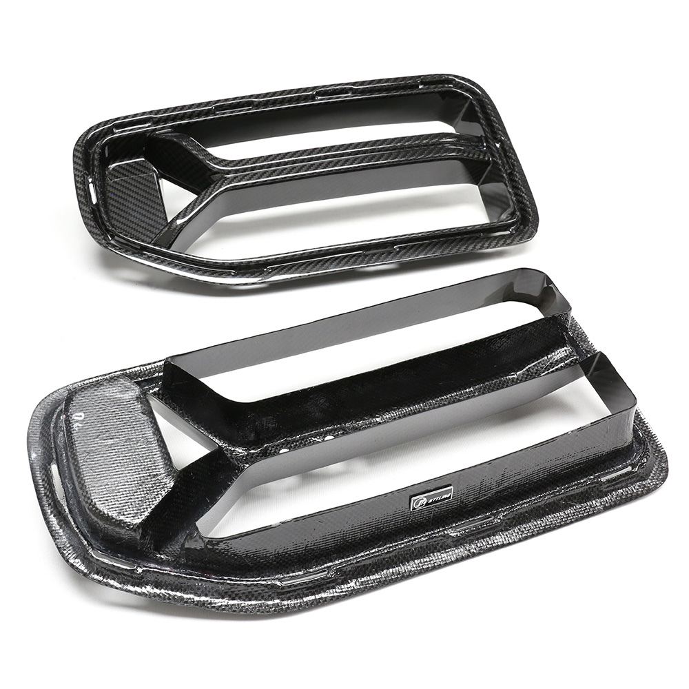 Two black carbon fiber car hood vents lie on a white surface. Each vent has a rectangular shape with a textured finish and features the "RTMG" logo attached.