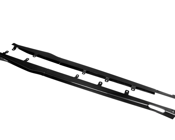 Two long, black carbon fiber side skirts lie flat with mounting brackets, displayed against a plain white background.
