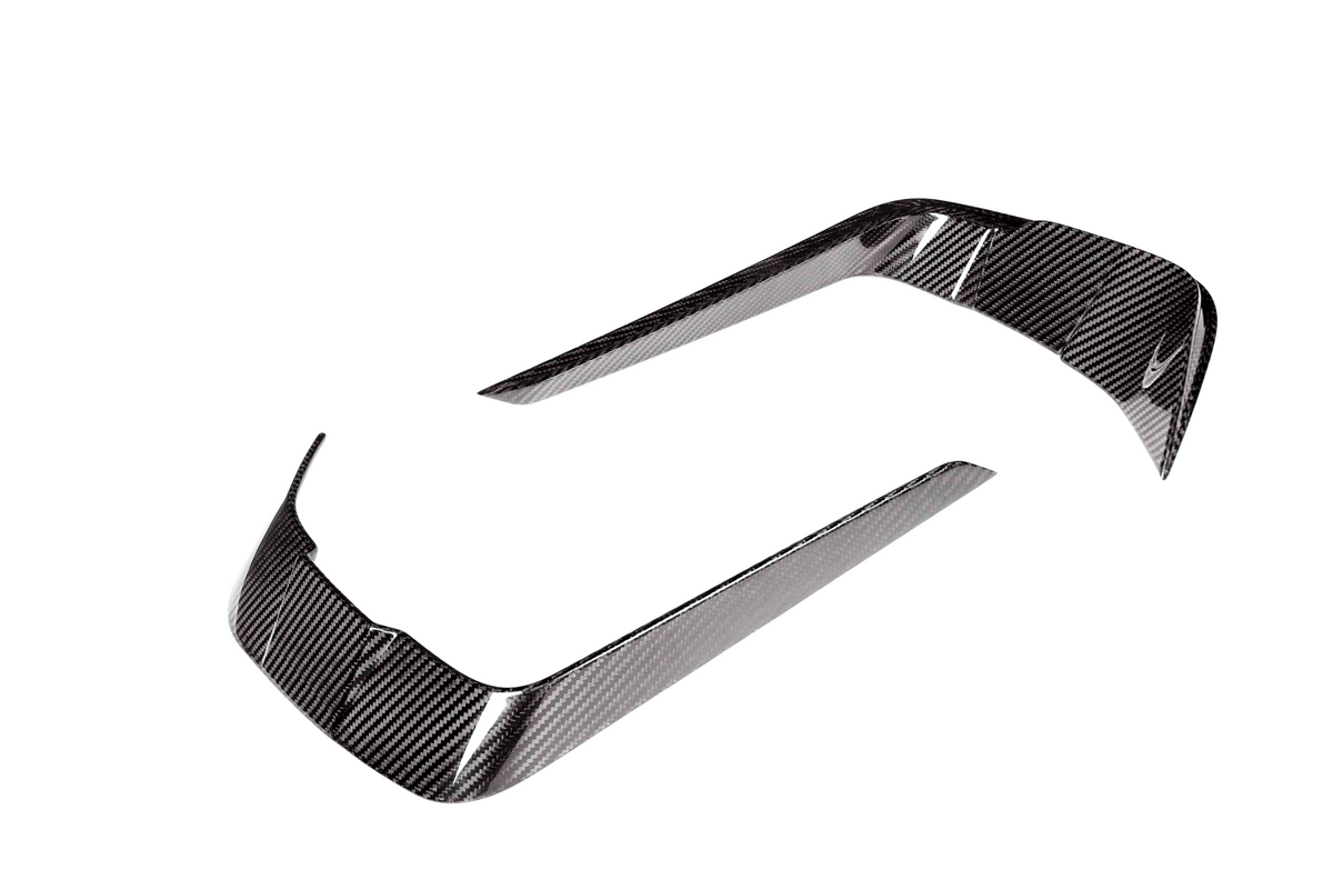 Two curved carbon fiber trim pieces, reflecting light, positioned apart on a white background. They are designed for vehicle detailing.
