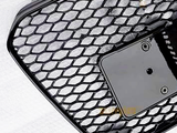 A black honeycomb grille with a smooth plate section sits against a textured white background. The grille features a grid pattern with a few mounting holes on the plate.
