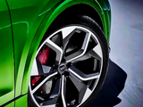 A green car features a close-up of its multi-spoke alloy wheel with red brake calipers. The car is positioned on a smooth, blue-toned surface.