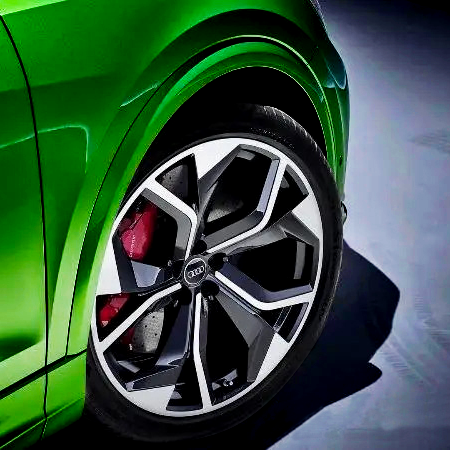 A green car features a close-up of its multi-spoke alloy wheel with red brake calipers. The car is positioned on a smooth, blue-toned surface.