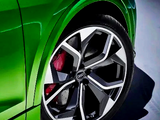 A shiny green car features a close-up of a stylish, geometric alloy wheel with a visible red brake caliper. The vehicle is positioned on a smooth, dark surface.