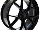 A glossy black alloy wheel is positioned upright, showcasing a multi-spoke design. The background is plain white, highlighting the wheel's sleek and modern appearance.