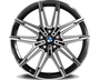 A polished, multi-spoke car wheel rim with a central BMW logo rests against a white background. The design features intricate, symmetrical patterns with alternating black and metallic finishes.