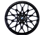 A black, multi-spoke alloy wheel with a central BMW logo, displayed against a plain white background, showcasing intricate design and structure.