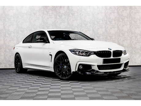 A white sports car with black rims is parked on a checkered floor in a minimalist setting with a light, textured wall backdrop.