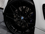 A black alloy wheel with a BMW logo is stationary, attached to a white vehicle on a textured, dark garage floor.