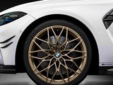 A gold alloy wheel with a BMW logo is mounted on a white sports car, with M Performance branding visible, set against a dark background.
