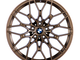 Bronze-colored, intricately designed car wheel with a multi-spoke pattern features a central BMW logo, highlighted in front of a plain white background.