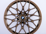 A bronze alloy wheel with intricate, multi-spoke design featuring the BMW logo in the center, set against a plain white background.
