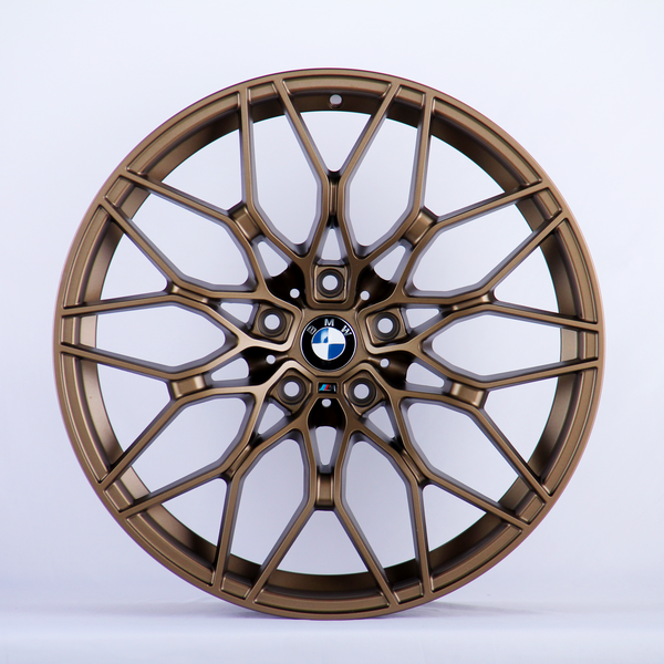 A bronze alloy wheel with intricate, multi-spoke design featuring the BMW logo in the center, set against a plain white background.