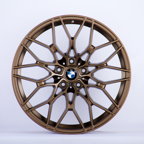 A bronze alloy wheel with intricate, multi-spoke design featuring the BMW logo in the center, set against a plain white background.