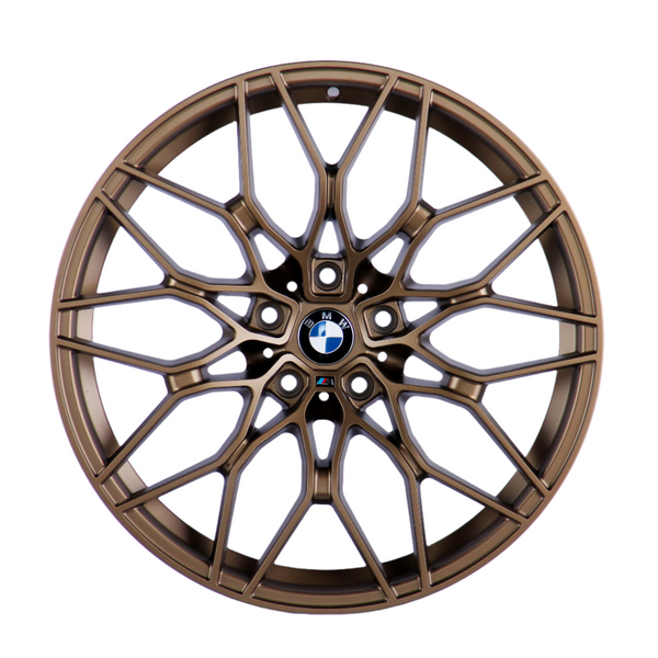 Bronze car wheel with intricate, multi-spoke design, centered on a logo featuring black, white, and blue colors, resting against a plain white background.