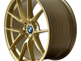 A gold alloy car wheel with a multispoke design features a central BMW logo. It sits isolated on a white background. Text on the rim reads “M PERFORMANCE.”