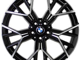 A metallic, multi-spoke alloy wheel with BMW logo at the center, designed for vehicles, displayed against a white background. The spokes feature a black and silver finish with intricate angles.