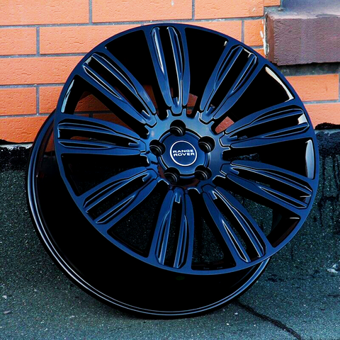 A glossy black Range Rover wheel rests against a red brick wall, showcasing intricate spokes. The central emblem reads "RANGE ROVER" in bold letters.