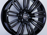 A black alloy wheel with a multi-spoke design rests on a gray pedestal. The center is embossed with 