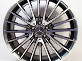 A silver and black alloy wheel with a Mercedes-Benz emblem and an AMG badge, featuring multiple spokes, positioned against a plain white background.