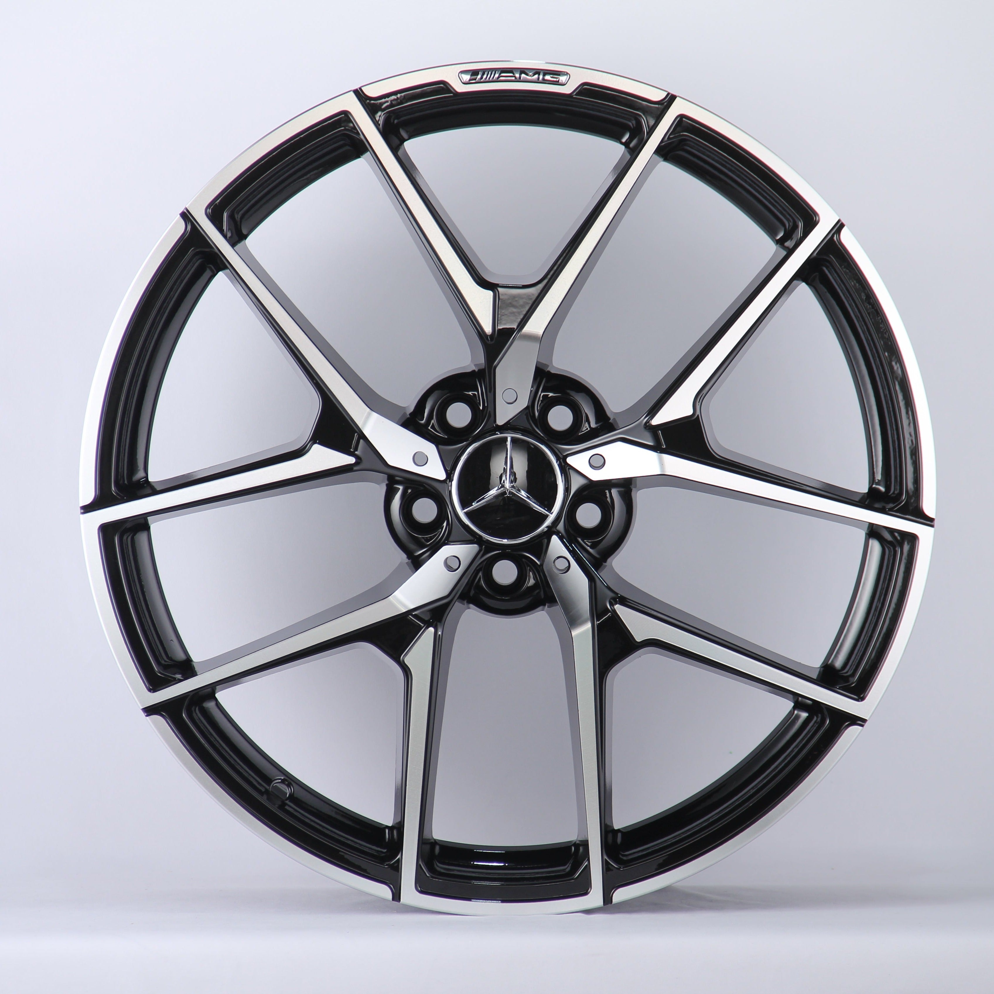 A metallic Mercedes-Benz wheel rim with five intricate spokes showcases the AMG logo, set against a plain white background.