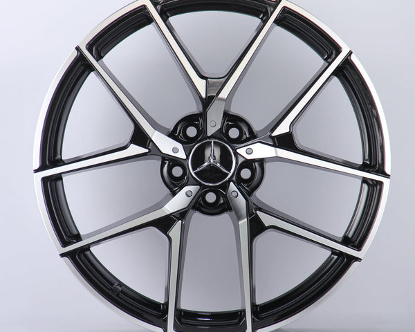 A metallic Mercedes-Benz wheel rim with five intricate spokes showcases the AMG logo, set against a plain white background.