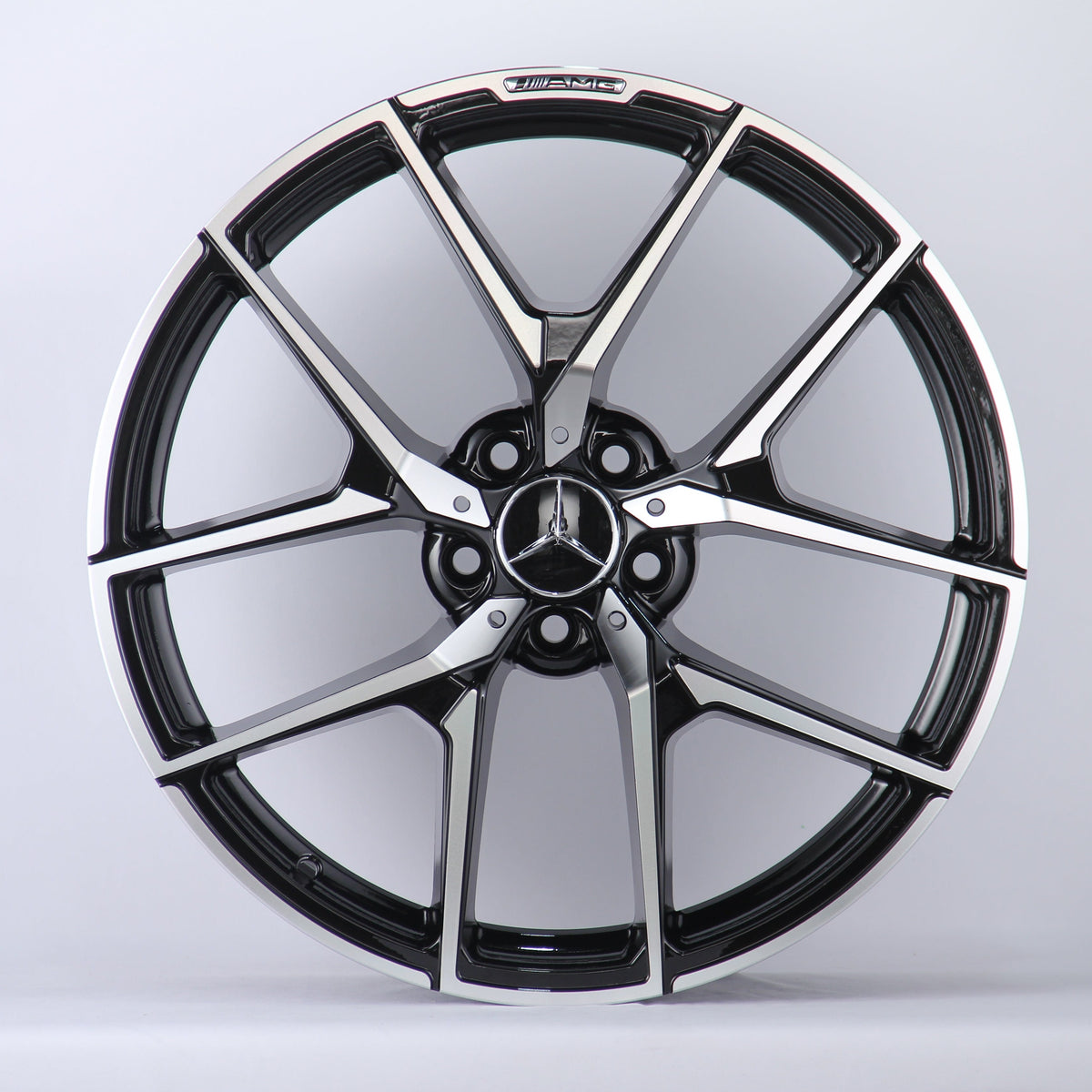A metallic Mercedes-Benz wheel rim with five intricate spokes showcases the AMG logo, set against a plain white background.