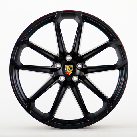 A black alloy wheel with multiple spokes and a central emblem displaying "Porsche" logo, seen on a plain white background.