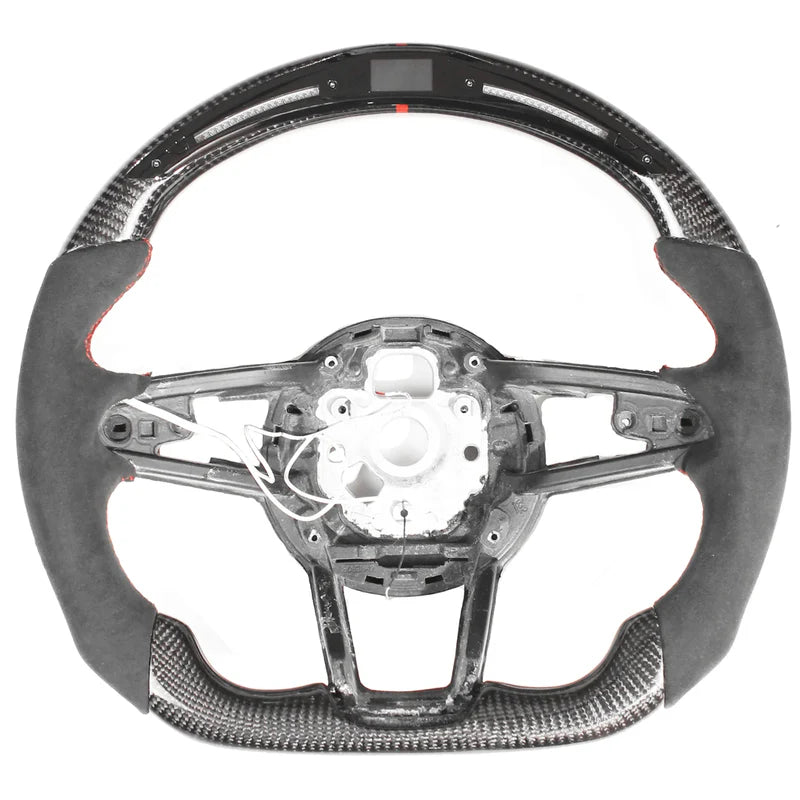 Steering wheel, disassembled, showing a sleek design with carbon fiber and suede accents; some internal wiring is exposed, against a plain white background.
