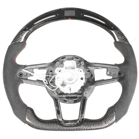 Steering wheel, disassembled, showing a sleek design with carbon fiber and suede accents; some internal wiring is exposed, against a plain white background.