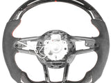 A steering wheel with an exposed interior structure, featuring carbon fiber details and a digital display at the top. The wheel is set against a plain white background.