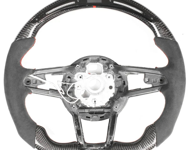 A steering wheel with an exposed interior structure, featuring carbon fiber details and a digital display at the top. The wheel is set against a plain white background.