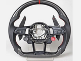 A carbon fiber car steering wheel, with multiple buttons including “VIEW” and “MENU” on the left and “RES” on the right, is displayed on a stand with a minimal background.