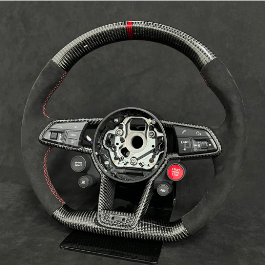 A carbon fiber steering wheel with black and red accents is displayed against a dark background. It features several buttons including "drive mode" and "START ENGINE STOP."