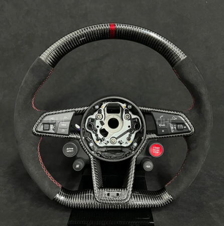 A carbon fiber steering wheel with red accents and buttons labeled "DRIVE MODE" and "START ENGINE STOP" is mounted upright against a dark background.