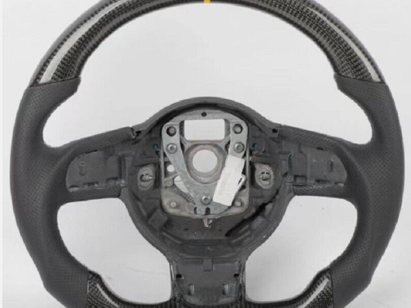 A carbon fiber steering wheel with a yellow center stripe, featuring a perforated grip, is set against a plain white background.
