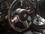 A carbon fiber steering wheel with a BMW logo is prominently displayed; it is part of a modern car interior featuring a dashboard and gear shift with sunlight illuminating the area.