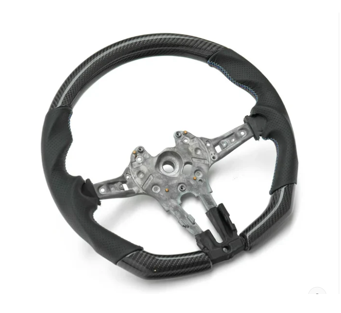 A black steering wheel with metal framework, featuring blue stitching and carbon fiber-like texture, rests on a plain white background.