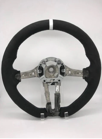 A circular car steering wheel with a visible metal framework is standing upright. It lacks a central cover, revealing internal fittings, and rests against a plain white background.