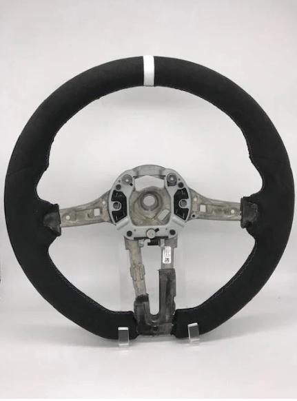 A circular car steering wheel with a visible metal framework is standing upright. It lacks a central cover, revealing internal fittings, and rests against a plain white background.