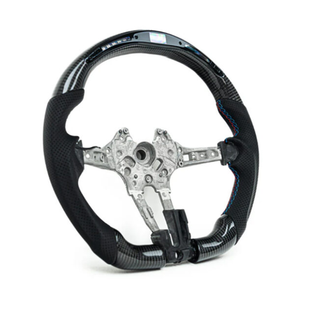 A black carbon fiber steering wheel with a metal frame is displayed against a white background. Blue stitching accents the grip areas, highlighting the sleek, sporty design.