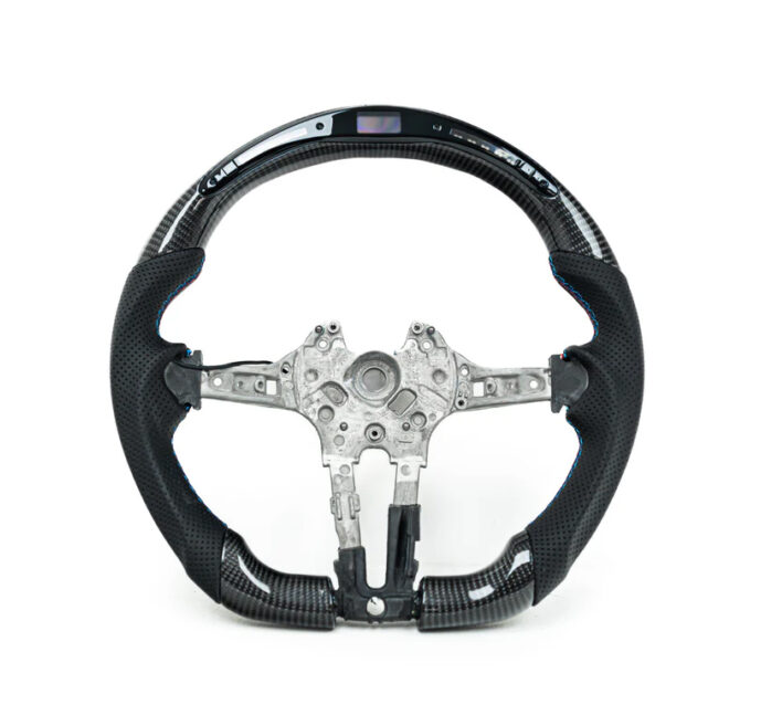 A carbon fiber steering wheel with metal interior components is displayed against a white background. Some buttons and an embedded digital display are visible on the upper section.