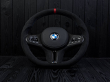 A black BMW steering wheel, showing control buttons on both sides and a central logo, is set against a dark wood-paneled background. Text includes: 