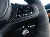 Steering wheel featuring textured grip, control buttons for phone, voice, and volume on carbon-fiber panel. Blue stitching detail, 'Evolve' tag visible, inside a car interior.