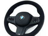 A black BMW steering wheel with control buttons, featuring a carbon fiber design and 