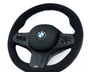 A black BMW steering wheel with control buttons, featuring a carbon fiber design and "M" logo, is set against a plain white background.