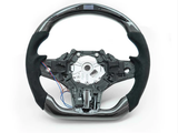 A car steering wheel, featuring carbon fiber detailing and exposed wiring, is set against a plain white background.