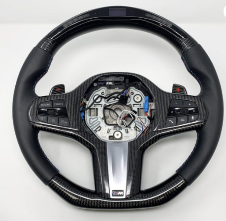A carbon-fiber and leather car steering wheel, with integrated buttons and exposed wiring in the center, set against a plain white background.